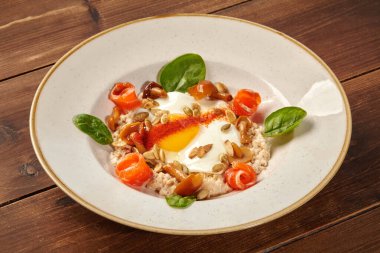 Tahta bir masada servis edilen kızarmış yumurta, somon, mantar ve sebzeli yulaf lapası içeren sağlıklı ve lezzetli bir kahvaltı.