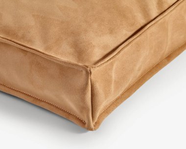 Sıcak bej renkli yumuşak süet yastık, dikişlerin işçiliğini ve lüks dokusunu vurguluyor.