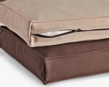 Bej ve kahverengi su geçirmez açık hava yastık kılıfları istiflenmiş, biri fermuar kapağını gösteriyor.