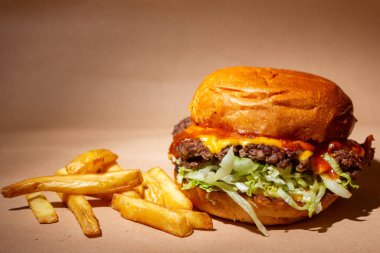 Altın hamurlu çok lezzetli bir hamburger, sulu et, salata, bir dilim erimiş peynir ve ketçap, yanında da altın patates kızartması.