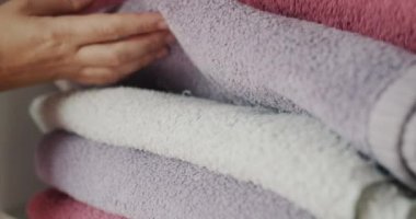 Womens fingers sort through clean towels on a shelf in the closet.