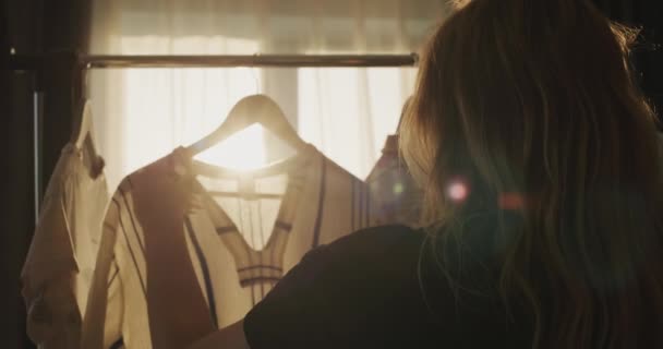 夕日の光の中で彼女の服を選択する女性のシルエット — ストック動画