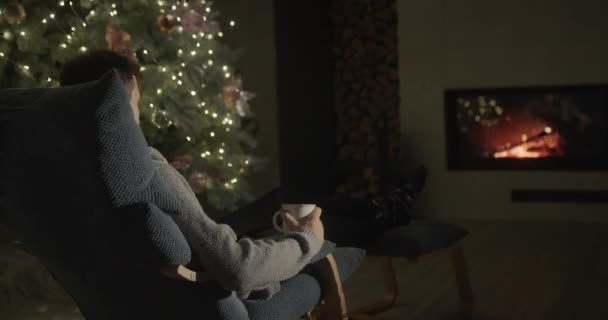 Mladý Muž Šálkem Čaje Odpočívá Krbu Vánočního Stromku — Stock video