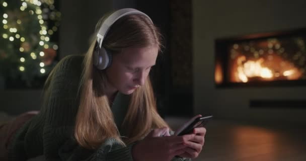 Een Meisje Met Een Koptelefoon Gebruikt Een Smartphone Ligt Vloer — Stockvideo