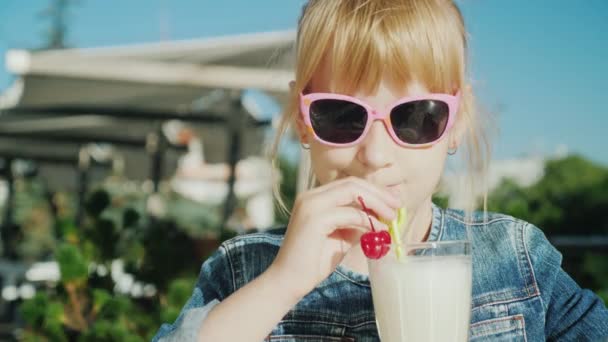 ピンクのメガネをかけた面白い女の子は カフェのサマーテラスでカクテルを飲みます 子供の概念で休む — ストック動画