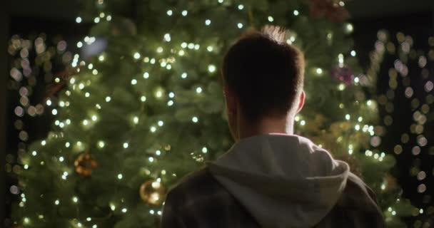 Ein Junger Mann Schmückt Hause Den Silvesterbaum Hängt Ein Spielzeug — Stockvideo