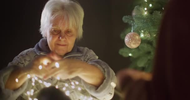 Пожилая Активная Женщина Распускает Гирлянду Возле Новогодней Елки Здоровый Активный — стоковое видео