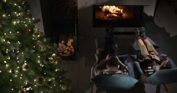 一个男人和一个女人坐在壁炉边喝茶 附近有一棵闪闪发光的圣诞树 平安夜 — 图库视频影像