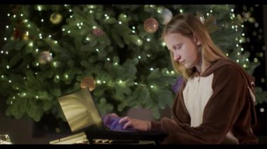 Geyik kostümlü bir genç evdeki büyük bir Noel ağacının arka planında dizüstü bilgisayar kullanıyor..