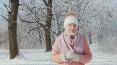 Orta yaşlı bir kadın açık bir günde bir kış parkında yürüyor, kar yağıyor. 4k yavaş çekim video