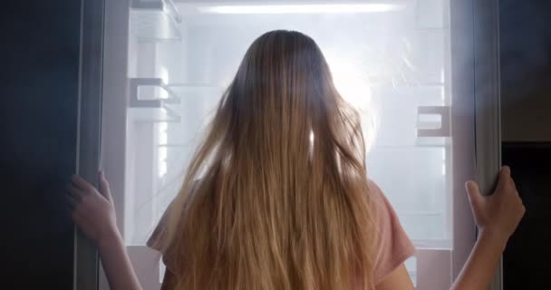 Una Mujer Joven Mira Refrigerador Abierto Donde Brilla Luz Viene — Vídeo de stock
