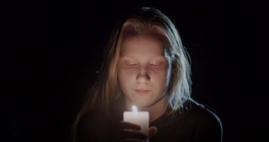 Karanlıkta yanan bir muma bakan bir çocuğun portresi..