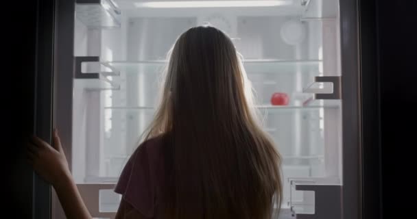 若い女の子は赤いリンゴが1つある空の冷蔵庫を見ています ダイエットと減量の概念 — ストック動画
