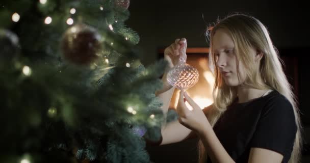 子供は手に美しいクリスマスのおもちゃを持っています 大きなクリスマスツリーのそばに座って 暖炉の火が背景に燃えています — ストック動画