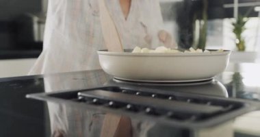 A woman fries potatoes on an induction electric stove with a built-in extractor fan.