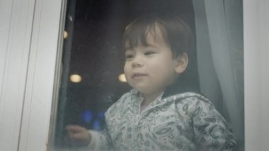 A two-year-old Azait boy looks out of the window, emotionally points his finger down.