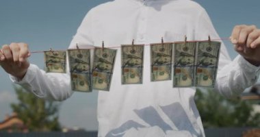 A man holds a clothesline in his hands, on which banknotes hang. Money laundering concept.