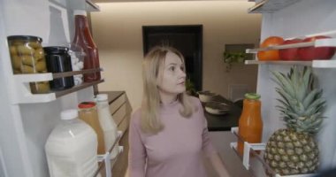 The woman takes an apple from the refrigerator. Light snack, view from inside the refrigerator.