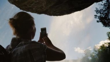 Bir şelalenin altında duran bir kadın Steinsdalsfossen fotoğrafını çeker ve üzerinde bir taş asılı durur. Norveç 'in görkemli doğası. 4K video