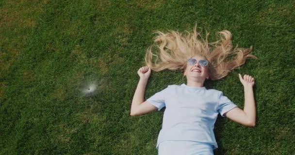 長い髪の子供は 水のジェットの下の芝生の上にあり 激しい熱から逃れる — ストック動画