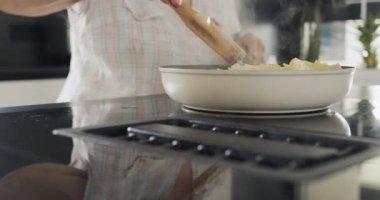 A woman fries potatoes on an induction electric stove with a built-in extractor fan.