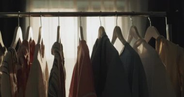 Omuzlarında kadın giysileri olan raflar. Pencereden parlayan batan güneşin ışınlarında.