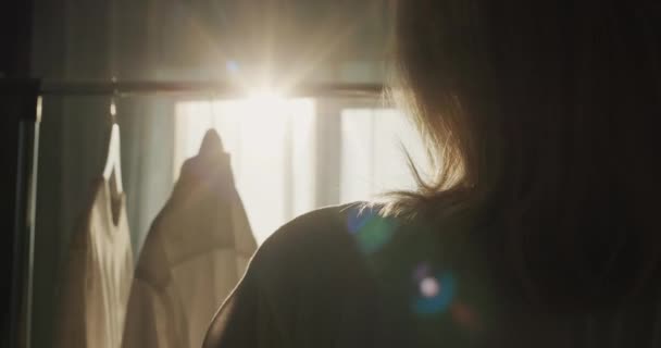 Femeie Atârnă Haine Raft Silueta Luminează Frumos Soarele Fereastră — Videoclip de stoc