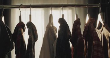 Rack with hangers with clothes in the rays of the setting sun that shines from the window.