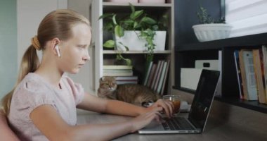 The child is engaged with a laptop in her room, next to her is a red cat.