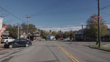 Mashana küçük bir Amerikan kasabasının merkez caddesinden geçiyor. Dükkan binaları, yol işaretleri ve evler görünür.