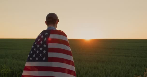 若いです男性農家です彼の肩の上にUsaフラグは 小麦畑の上に日の出を見て — ストック動画