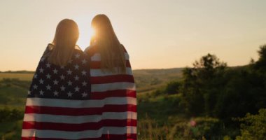 Omuzlarında Amerikan bayrağı taşıyan genç bir kızı olan bir anne resimli bir vadide güneşin batışını seyrediyor..