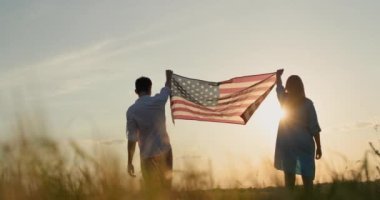 Bir adam ve bir kadın güneş batarken buğday tarlasının üzerinde Amerikan bayrağını göndere çekiyor. ABD 'nin bağımsızlık günü kavramı.