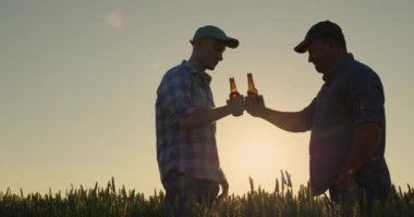 İki adamın siluetleri, bira şişelerini tokuşturur ve soğuk bir içecek içerler..