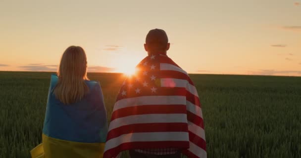 一个男人和一个女人 拿着乌克兰和美国的国旗 肩并肩地站在一边 望着麦田上的日出 — 图库视频影像