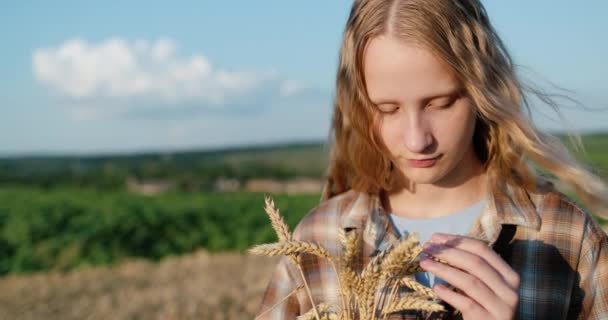 一个手里拿着麦穗的少女的画像 在风景如画的乡村和麦田的背景下矗立着 — 图库视频影像