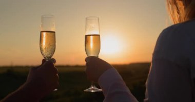 Ellerinde şampanya bardakları, güneşin battığı güzel bir manzaranın arka planına çarpıyor..