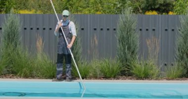 Tulumlu bir işçi evin arka bahçesindeki havuzu süpürüyor..