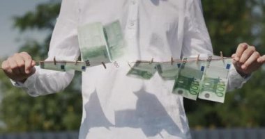 A man holds a clothesline in his hands, on which banknotes hang. Money laundering concept.