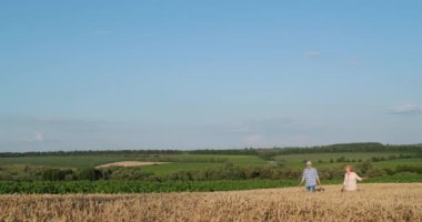 Two farmers walk through the picturesque countryside along a field of yellow wheat.