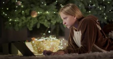 Geyik kostümlü bir genç evdeki büyük bir Noel ağacının arka planında dizüstü bilgisayar kullanıyor..
