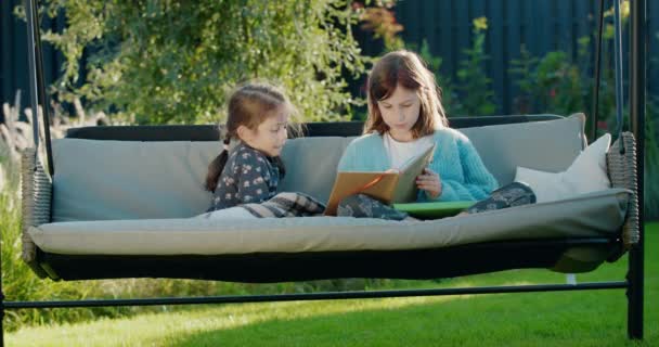 Mädchen Liest Ihrer Jüngeren Schwester Ein Buch Vor Und Entspannt — Stockvideo