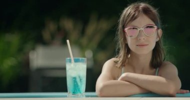 Havuzun kenarında güneş gözlüklü şirin bir kızın portresi. Yakınlarda soğuk bir kokteyl var..