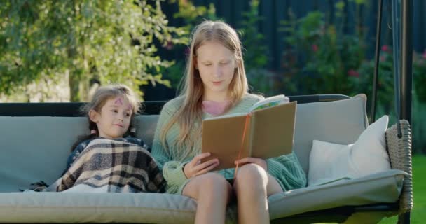 Een Tienermeisje Leest Een Boek Voor Aan Haar Jongere Zus — Stockvideo