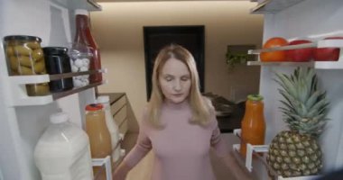 Çekici orta yaşlı kadın buzdolabından yiyecek kapları alıyor. Buzdolabının içinden bak. 4k video