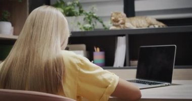 The child is engaged with a laptop in her room, next to her is a red cat.