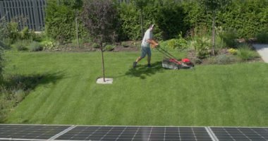 Bir adam evin bahçesinde çimleri biçiyor, kulaklıkla müzik dinliyor.