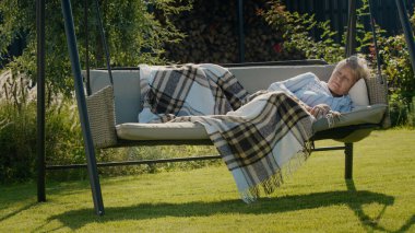 Yaşlı bir kadın bir evin arka bahçesindeki salıncakta uyuyor..