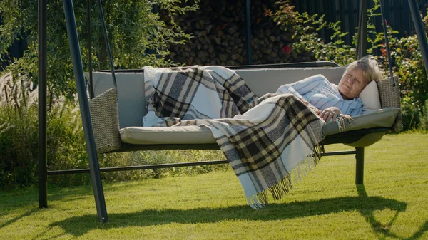 Yaşlı bir kadın bir evin arka bahçesindeki salıncakta uyuyor..