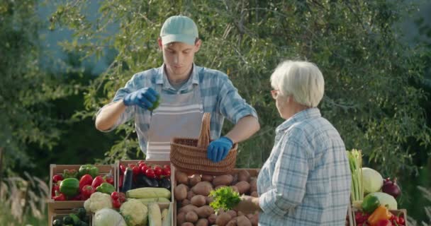Пожилая Женщина Покупает Овощи Фермерском Рынке Продавец Кладет Овощи Корзину — стоковое видео
